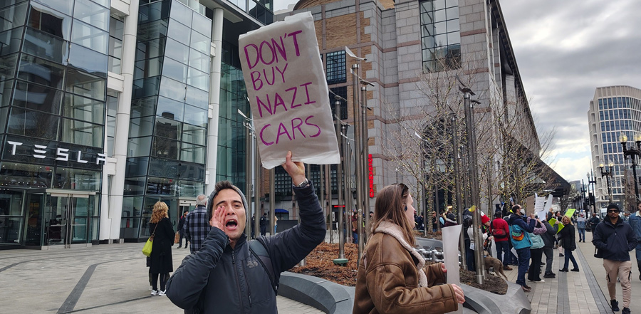 Protesters outside the Prudential Tesla showroom, including one holding a sign against Nazi cars