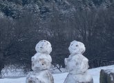 Snowmen at the top of Peters Hill in the Arboretum with downtown Boston and the Back Bay behind them