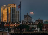 Sunlight reflects off one side of building while the moon goes down on the other