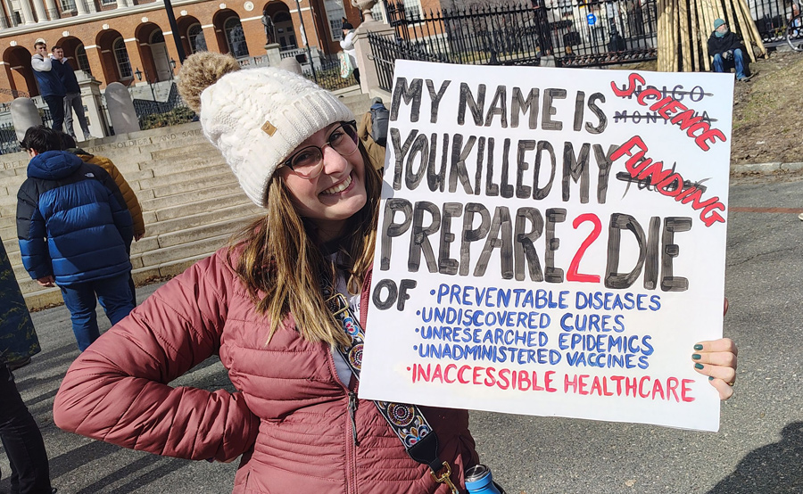 Woman with sign saying My Name is Science, You Killed My Funding, Prepare to Die, of various things